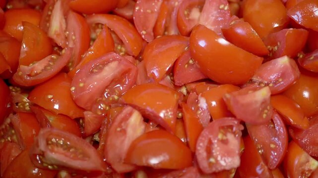 Slow motion pan over a large pile of fresh chopped red tomato wedges showing seeds and juice. This macro footage illustrates ingredient preparation for healthy cooking or salsa.
