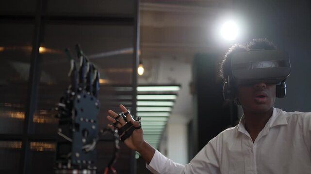 Young man in VR headset touches a robotic hand in a dim room