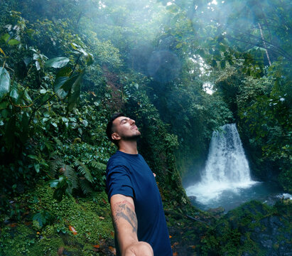 Man with closed eyes embracing nature while standing near a waterfall in the lush, green jungle of Arenal Volcano National Park