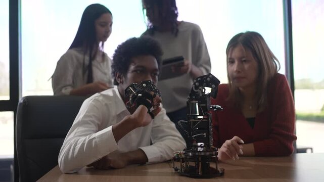 Students examine a sensor glove and robotic arm in a bright room