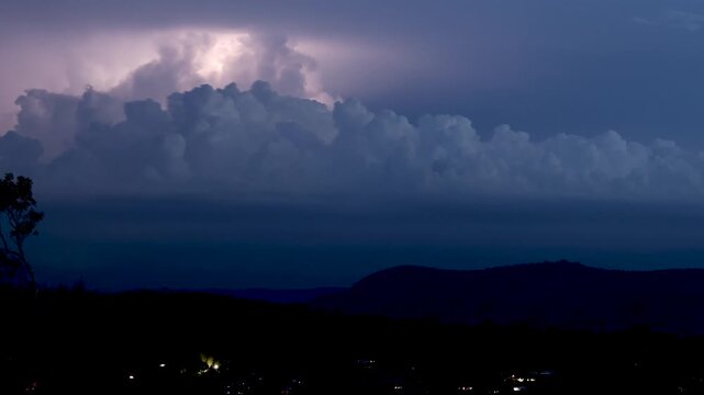 Thunderstorm at night with lightning strikes flashing behind dark clouds over hills.