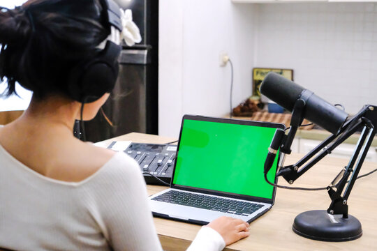 Female Content Creator Recording Podcast at Home with Laptop Green Screen and Professional Microphone Setup