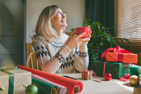 Woman enjoying a hot drink from a red mug at home.
She takes a cozy holiday break with a warm beverage, creating a festive Christmas lifestyle scene.