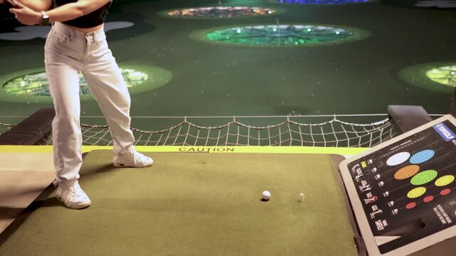 Woman swings golf club at driving range hitting ball, dynamic action shot.