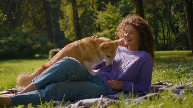 Happy Caucasian woman female pet owner training golden welsh corgi dog on grass in summer park playing outside. Young girl feeding active playful puppy with treats animal trainer exercising smart pup
