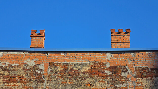 Weathered red brick building wall and two decorative chimneys on a sunny day