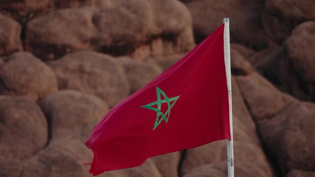 The Moroccan flag waves proudly in the wind, set against a backdrop of rugged rocks. This captivating scene evokes a sense of place and national identity, perfect for travel or cultural projects.