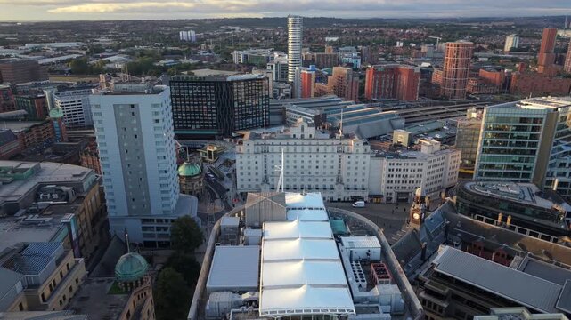 Aerial video overlooking Leeds city centre streets and architecture towards the railway station and skyline under morning Sun.