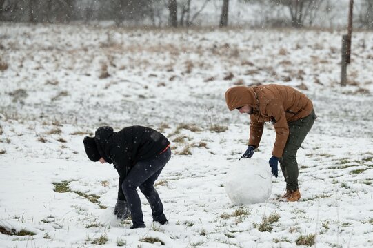 Two individuals build a snowman together in a snowy field, enjoying a winter day's playful activities.