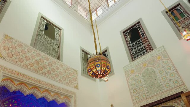 Traditional Moroccan courtyard with colorful ornate tile work. Beautiful hanging lamps illuminate the space, and intricate window grills create a mesmerizing ambiance. Moroccan architecture.
