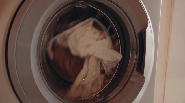 Clothes spinning in a washing machine. Laundry day, chores, and cleanliness. The concept of washing clothes and using a washing machine. The circular motion of the clothes and water inside the machine