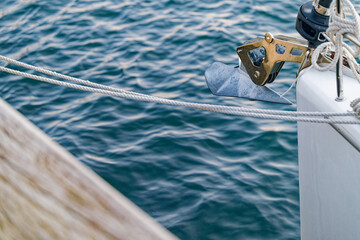 Boat anchor hanging on the side of a white yacht over blue water © Holger