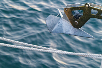 Metal boat anchor and white rope over calm blue water surface on a sailing vessel © Holger