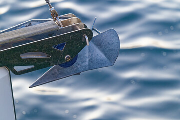 Metal boat anchor attached to a sailing vessel with calm water background © Holger