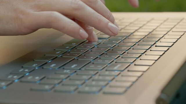 Close-up shot shows a woman typing the word Cava on a laptop keyboard. The setting is outdoors with natural light. Fingers move quickly across the keys.