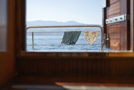 View from inside the ship of swimming trunks and swimsuit suspended to dry, in the background land, morning light, sailing ship, Aeolian or Aeolian Islands, Sicily, Southern Italy, Italy