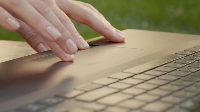 A woman uses her fingers to navigate the touchpad on a laptop. She then presses a key while working outdoors in a casual setting.