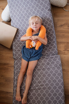  little girl sleeping peacefully on folding mattress holding orange travel neck pillow