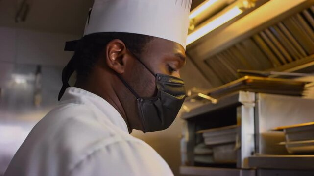 Black chef adjusts kitchen mask and chef hat before cooking, restaurant hygiene, food safety preparation, hospitality staffing, commercial kitchen readiness, culinary work focus, service standards.