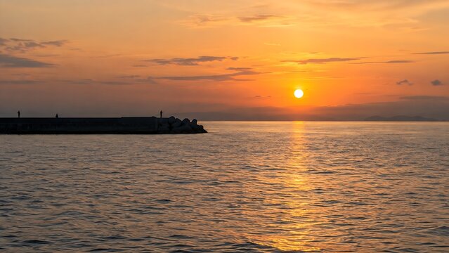 Sunset over the sea from a breakwater with silhouettes of anglers far in the distance