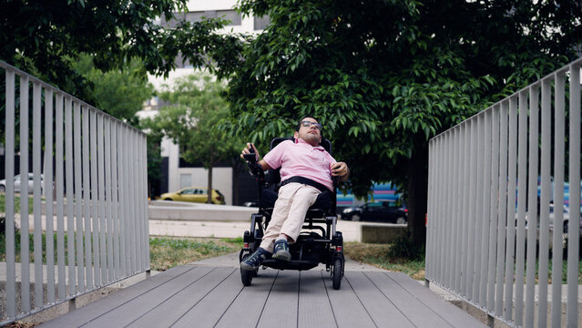 Man with physical disability using a motorized wheelchair, navigating an accessible ramp in an urban park. Demonstrating mobility and independence