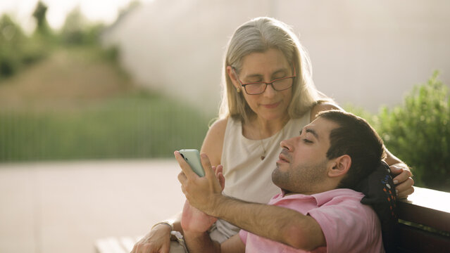 Man with spina bifida and a woman sitting outdoors, both looking at a smartphone, sharing a moment of connection and support