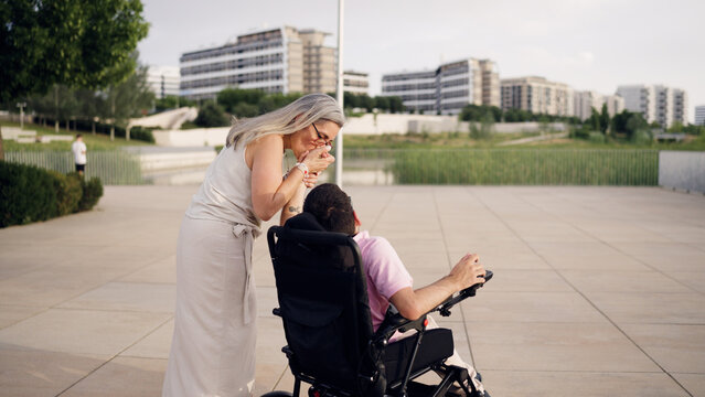 Loving mother showing affection to her adult son with spina bifida in an electric wheelchair outdoors in a city park