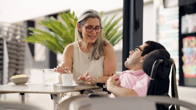 Caregiver assisting a disabled man in a power wheelchair, sharing a moment, promoting inclusion and support in a cafe setting
