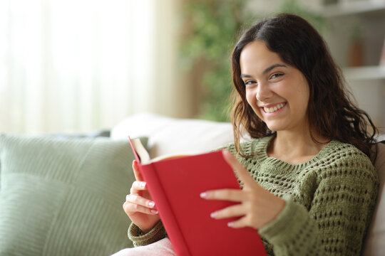 Happy young woman holding paper book looking at you