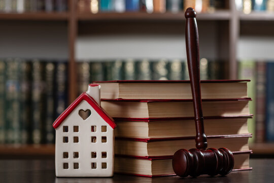 A judge's gavel and a symbolic house set against a backdrop of bookshelves.