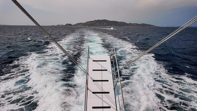 Panoramic view from the stern of a motorboat speeding across a rough, dark blue sea, leaving behind a wide, dynamic wake of white, foaming water.