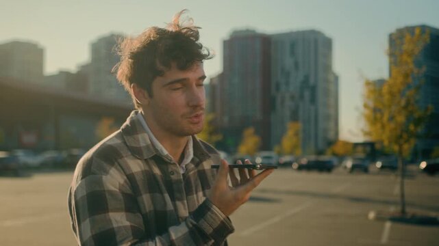 Young Caucasian business man walking in city recording voice message on mobile phone smiling businessman chatting online positive guy sending audio voicemail on speakerphone using smartphone outdoors