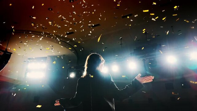 Successful female speaker celebrates triumph after a presentation on stage with falling confetti. Concept of public speaking, achievement, victory and professional success.