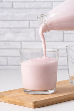 Pouring homemade fruit kefir, buttermilk or yogurt with probiotics. Yogurt flowing from glass bottle on light background. Probiotic cold fermented dairy drink. Trendy food and drink