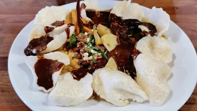 Pouring dark peanut sauce over traditional Indonesian tahu telor dish