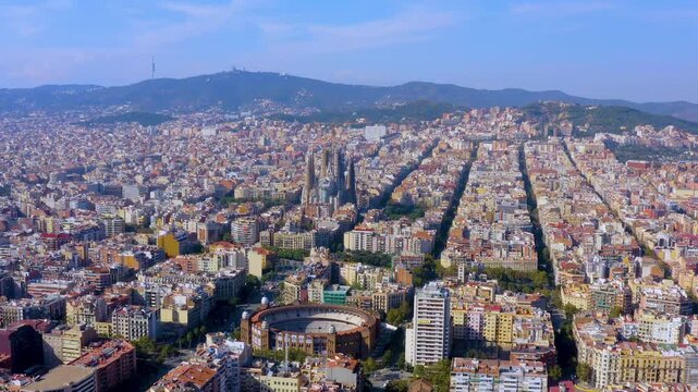 Aerial drone view of Barcelona with the Sagrada Familia basilica under construction, the Eixample street grid, La Monumental bullring and Tibidabo on the Collserola hills, Catalonia, Spain.