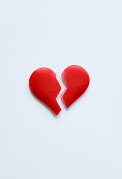 A red broken heart lies on a pale background with a visible split between its two halves. The concept represents heartbreak, separation and the end of a relationship