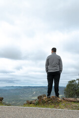 A man stands with his back to the camera, admiring the vast horizon framed by clouds and mountains from the top of a mountain pass. © LaSierragPhotoGraphy