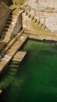 Water storage inside Toorji Ka Jhalra Baoli stepwell - one of water sources in Jodhpur, Rajasthan, India. Sunny day, water riffles reflect walls of the pool. Vertical panning down to up.