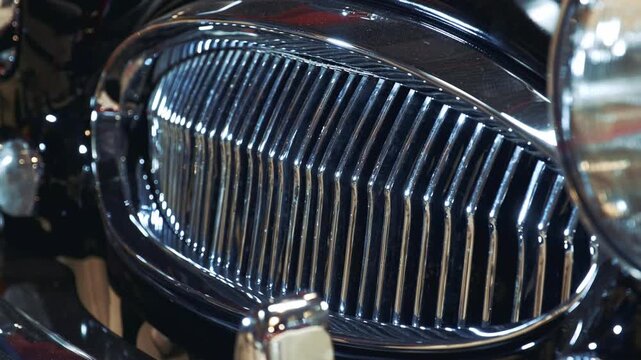 Extreme close-up of a shiny, chromed radiator grill and headlight on a black vintage luxury automobile, highlighting detailed textures and reflective surfaces.