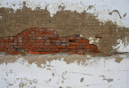 Deteriorating multilayer wall surface with chipped white paint and exposed concrete in a horizontal composition, revealing weathered red clay brick, cracked mortar, and white mineral deposits