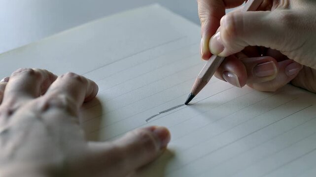 Lowering graphite pencil, adult hands drawing shaded mark along guidelines on desk