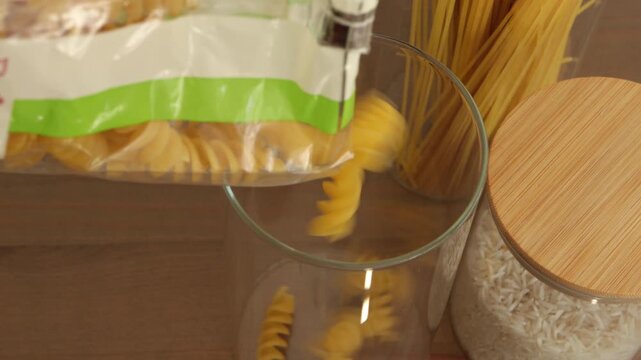 Pouring pasta in a glass storage jar. Organizing kitchen and pantry routine, with reusable containers used to store everyday food staples