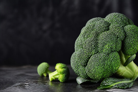 A head of broccoli rests on a dark, textured surface against a black background.