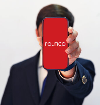 Illustrative editorial of person holding phone with politico app logo on screen in suit