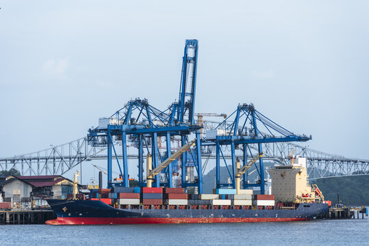 Large container ship berthed beneath gantry cranes during cargo loading operations at a modern container terminal.
