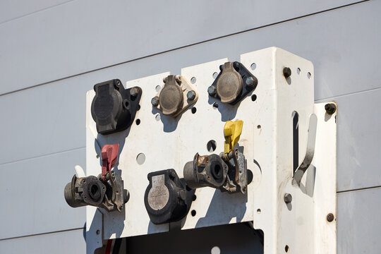 Truck semi-trailer front panel featuring red and yellow gladhand brake couplers, multi-pin electrical sockets, a safe coupling instruction decal, and various air hoses and cables, all mounted securely