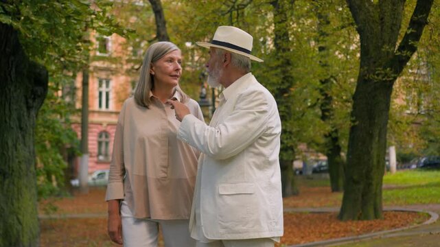 Happy loving Caucasian elderly couple holding hands talking walk in city park elegant senior married man and woman grandparents enjoying active retirement summer relaxation nature happiness outdoor