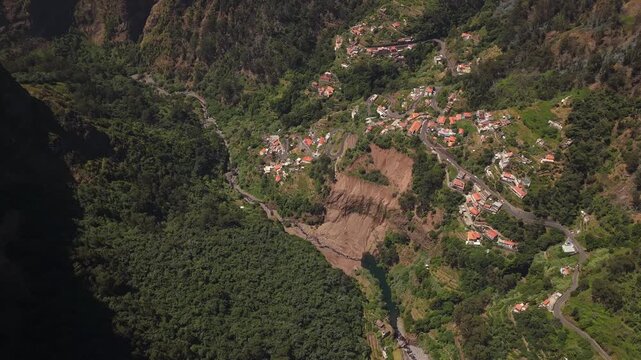 Drone video captures a dramatic landslide cutting through a lush hillside village with damaged terrain and scattered homes under bright daylight, highlighting the aftermath of heavy El Nino flooding.