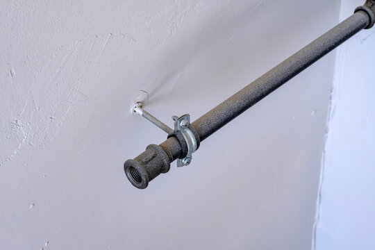 Metal pipe with clamp bracket. Pipe with threaded coupling secured to wall by a metal pipe clamp bracket. Suitable for plumbing, construction, and building maintenance editorial or commercial use.